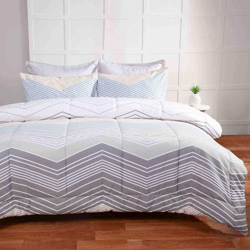 Bed with chevron patterned comforter and pillows in a room with wooden flooring.