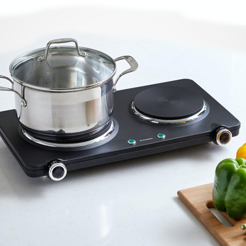 Portable electric stove with a pot on a white surface, surrounded by vegetables.