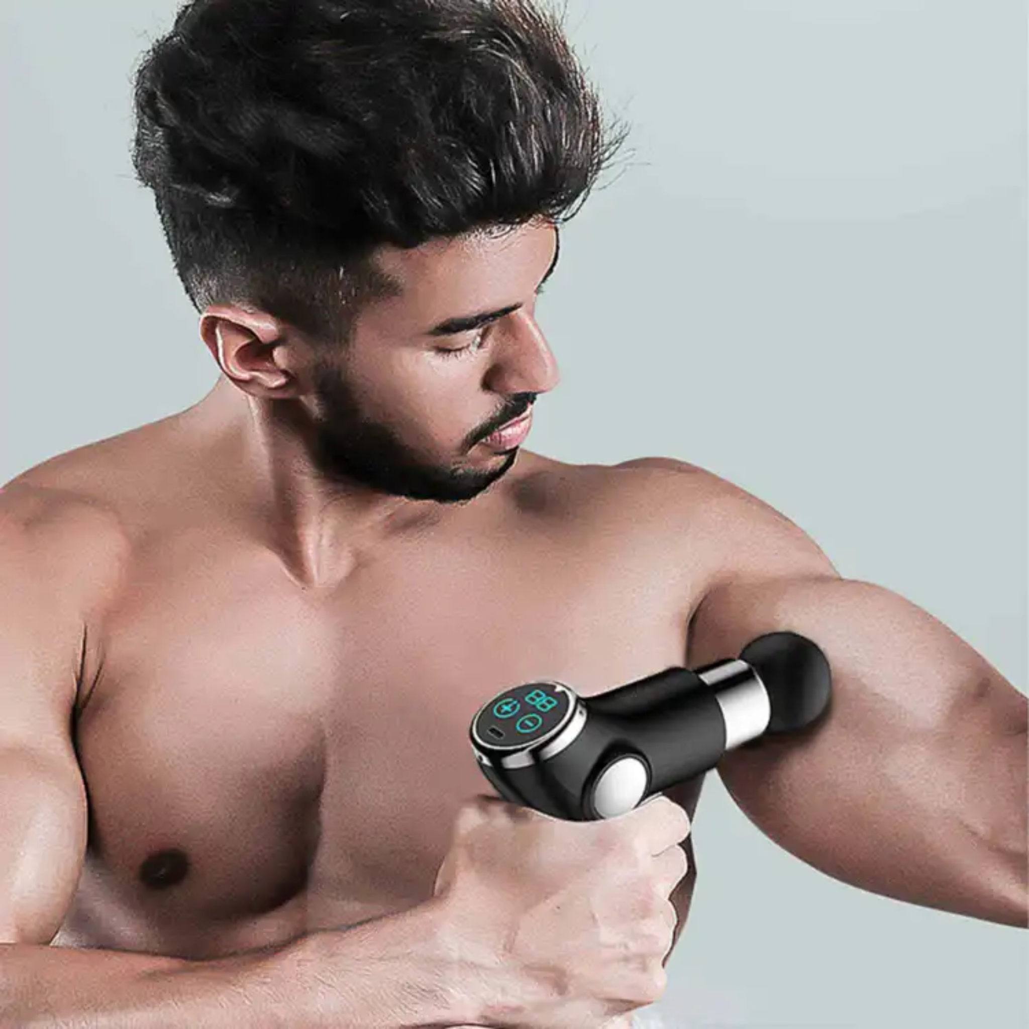 Man using a handheld massage device on his arm against a gray background