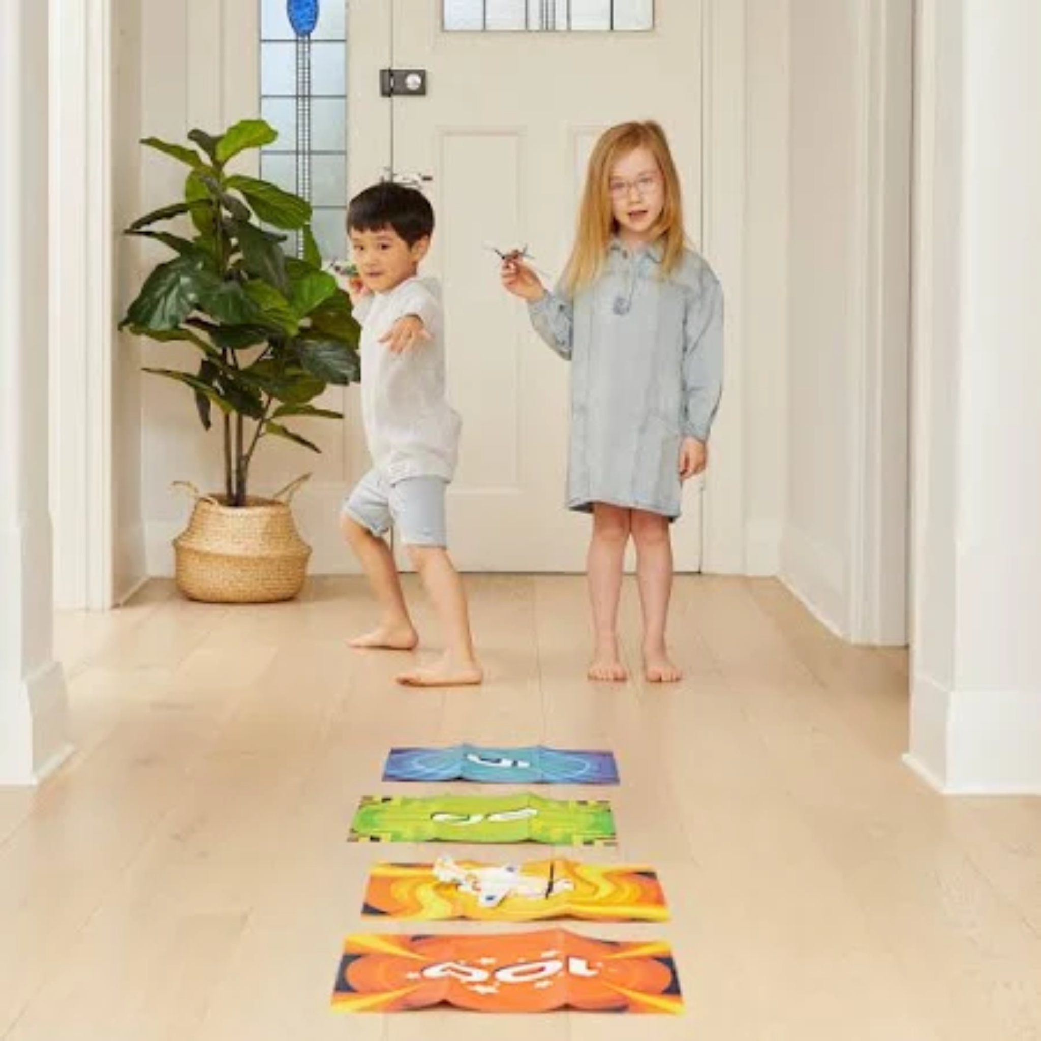 Two children playing with colorful mats on a wooden floor.