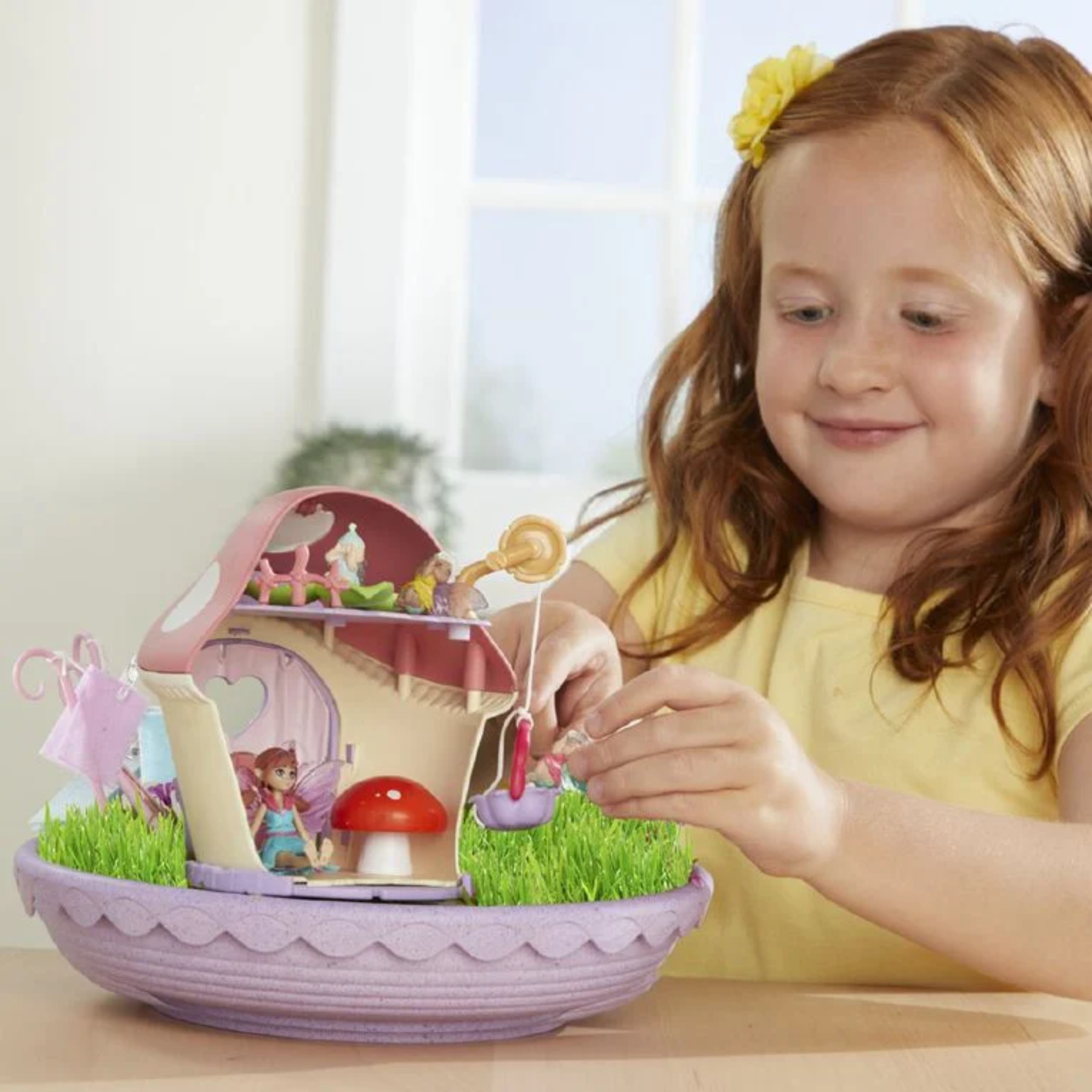 Young girl playing with a fairy garden toy set on a table.