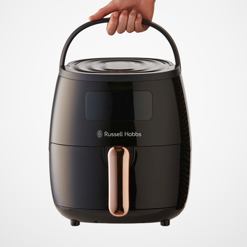 Black Russell Hobbs air fryer with a hand holding the handle on a white background
