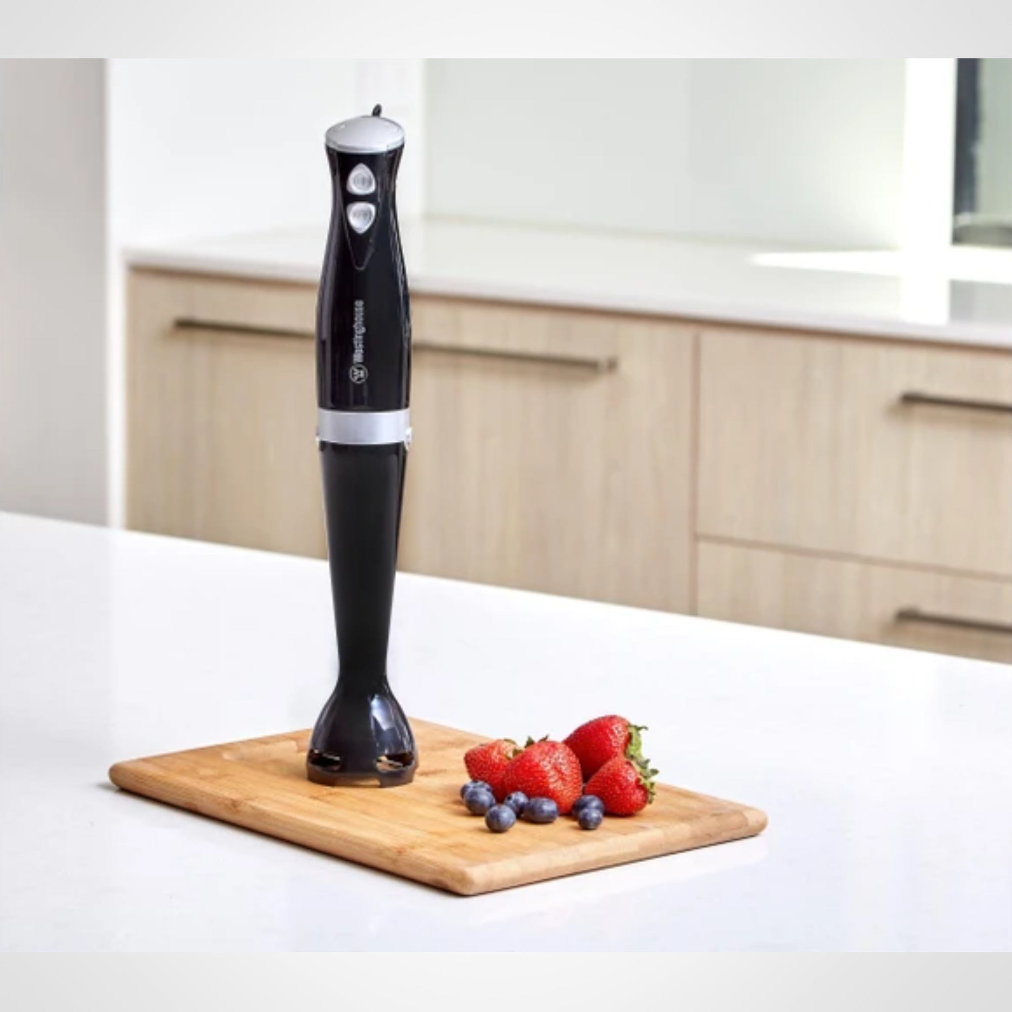 Black handheld blender on a wooden cutting board with strawberries and blueberries in a kitchen setting